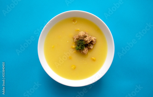 Corn cream soup in a white bowl isolated on blue background. Top view.