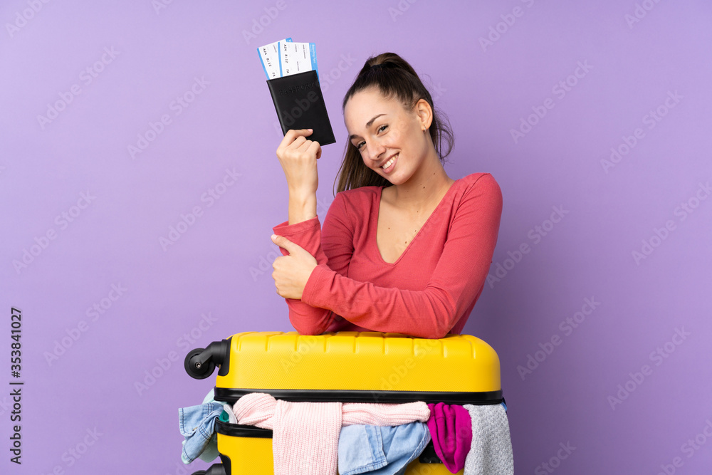 Traveler woman with a suitcase full of clothes and holding a passport over isolated purple background Traveler woman with a suitcase full of clothes and holding a passport over isolated purple background