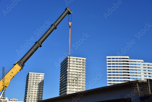 Crane hook on lifting gears and chains hanging of the mobile auto crane on a background residential building and blue sky. Concept of bridge construction