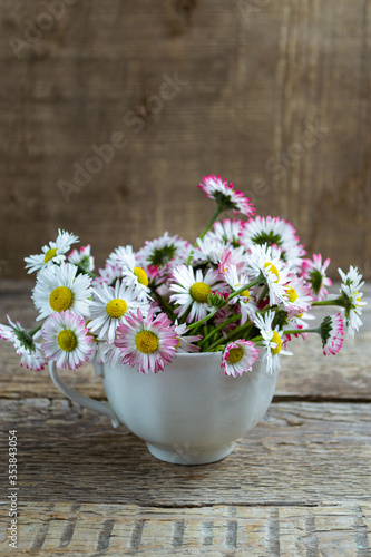 Bouquet of common daisies Bellis perennis in tea cup on a wooden table  rustic style. Selective focus.