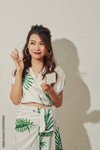 Beautiful asian girl in summer dress doing make-up with her small mirror and powder in sunny afternoon