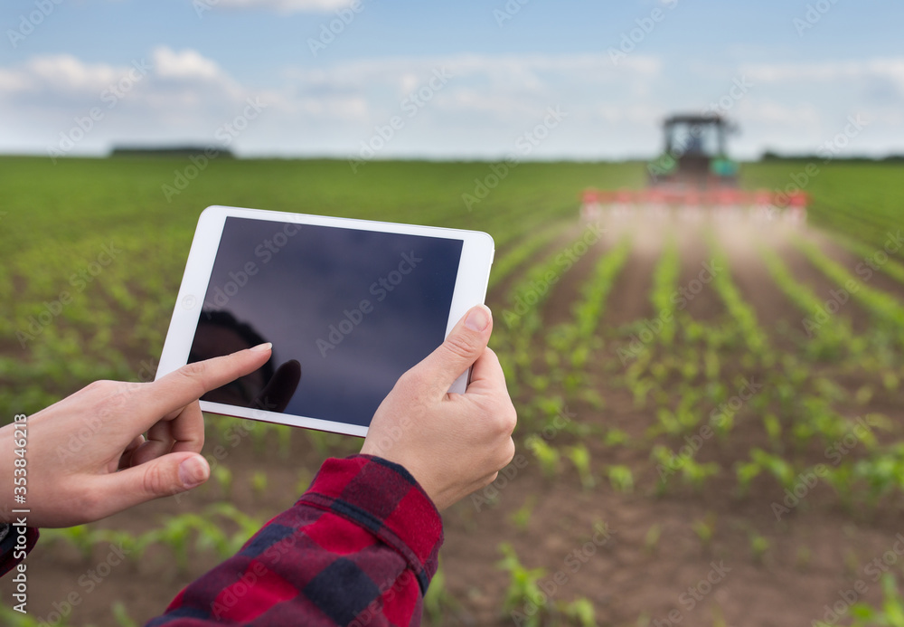 Farmer working on tablet in front of tractor in field