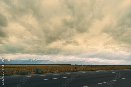 Landscape photo with a part of road, wheat and mountains on a cloudy day