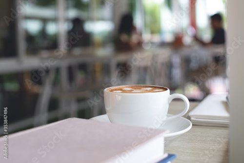Cup of coffee and books on table in coffee shop coworking space with nobody