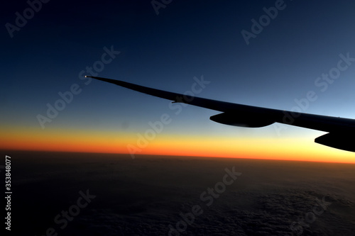 Silhouette of Airplan wing in twilight sky, with beautiful light from dramatic sunset, Romantic view from airplane window. 