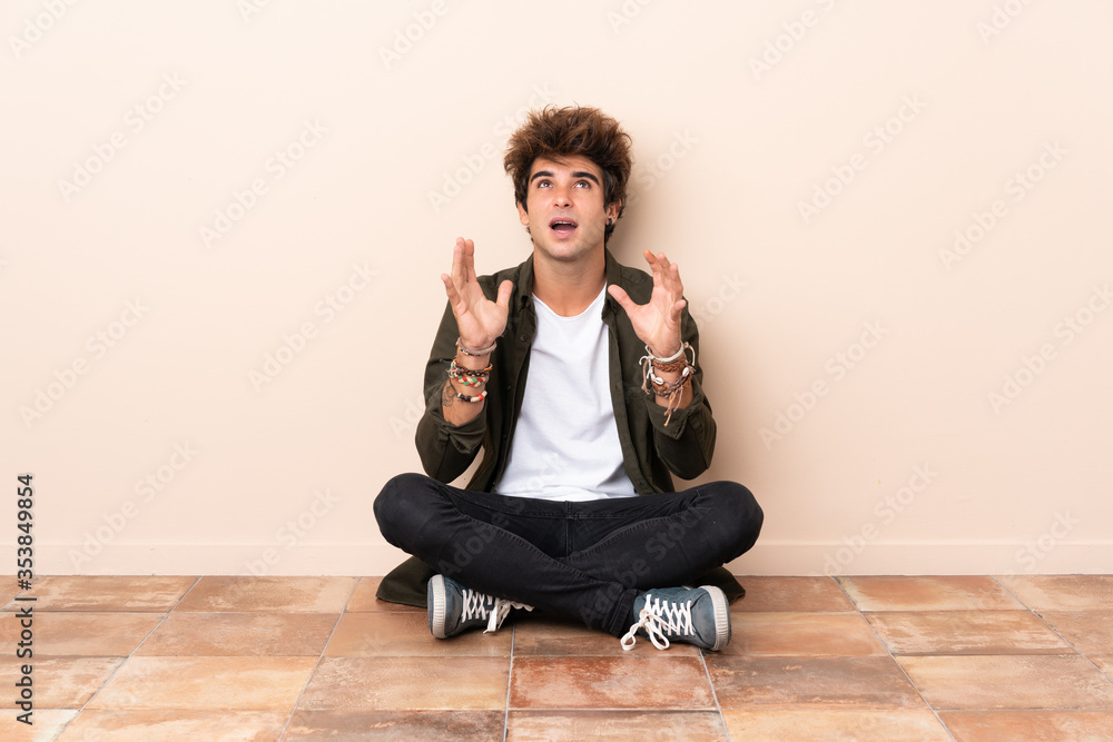 Young caucasian man sitting on the floor frustrated by a bad situation Young caucasian man sitting on the floor frustrated by a bad situation