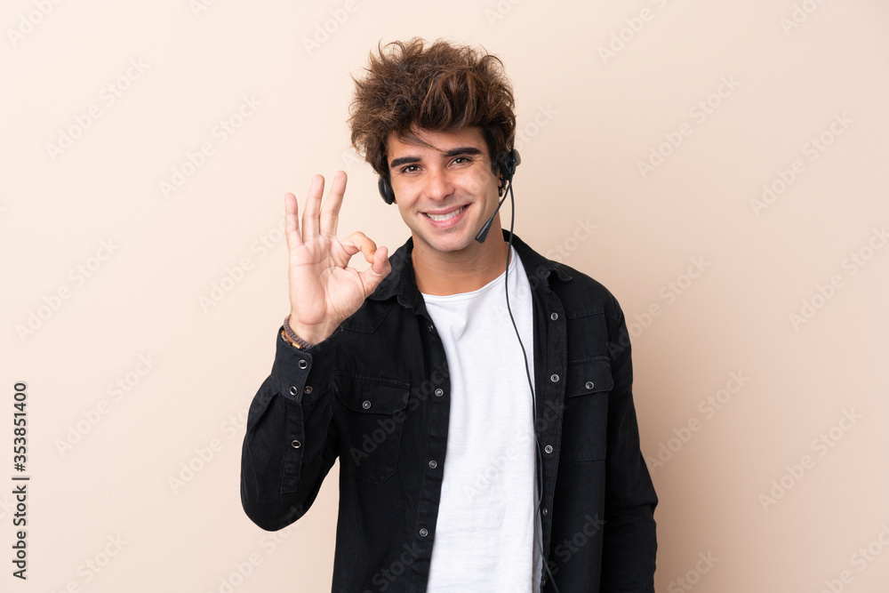 Telemarketer man working with a headset over isolated background showing an ok sign with fingers