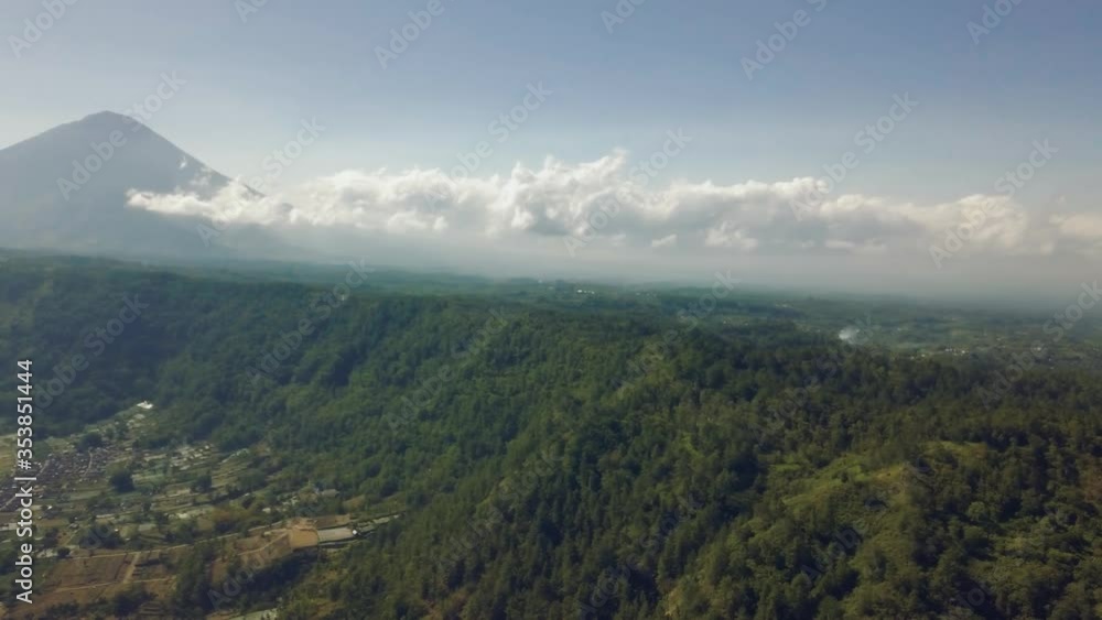 Panoramic aerial view of countryside village with beach, forest green mountains. Shot on cloudy summer day, white clouds above green forest mountain.