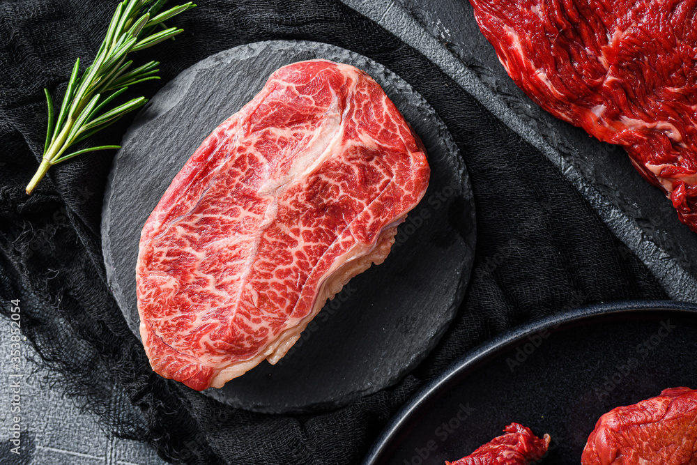 Raw top blade cut black angus organic  steak on a black plate and stone slate with seasonings, herbs  grey concrete background. Top view close up.