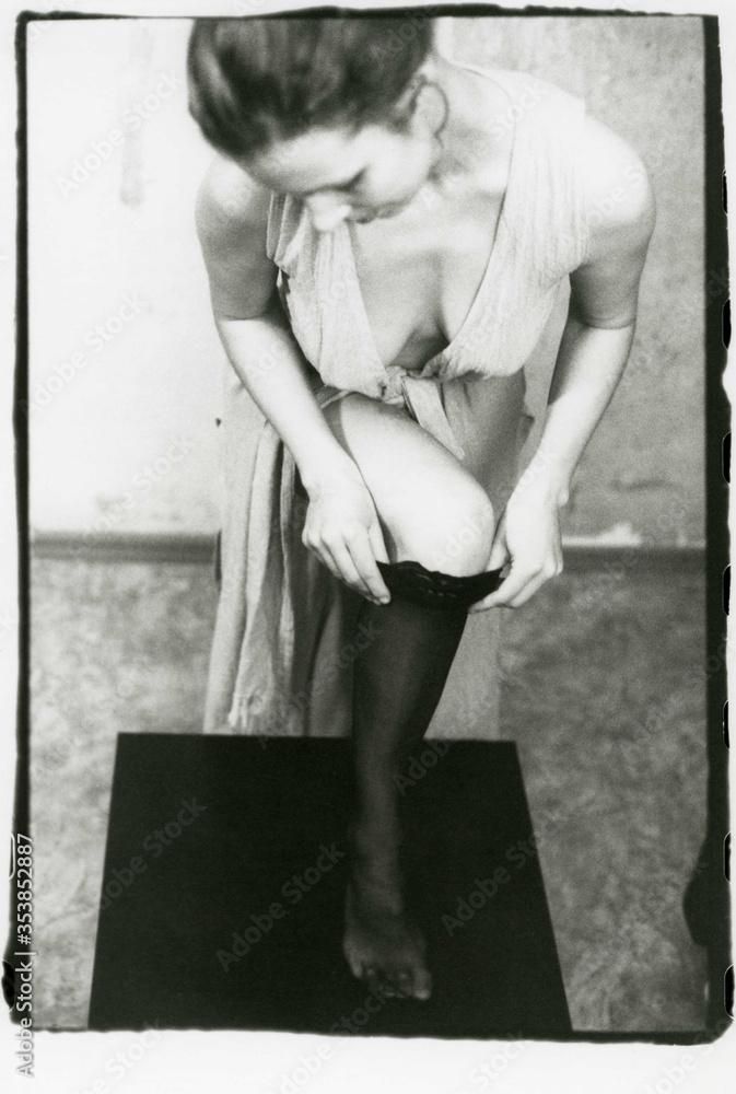 A young slender girl in clothes with a deep neckline puts on a stocking on her leg. A young slender girl in clothes with a deep neckline puts on a stocking on her leg.