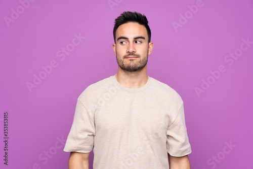 Young handsome man over isolated purple background making doubts gesture looking side © luismolinero