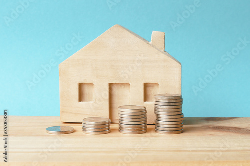 Vászonkép Piles of coins and a wooden  house on a blue background