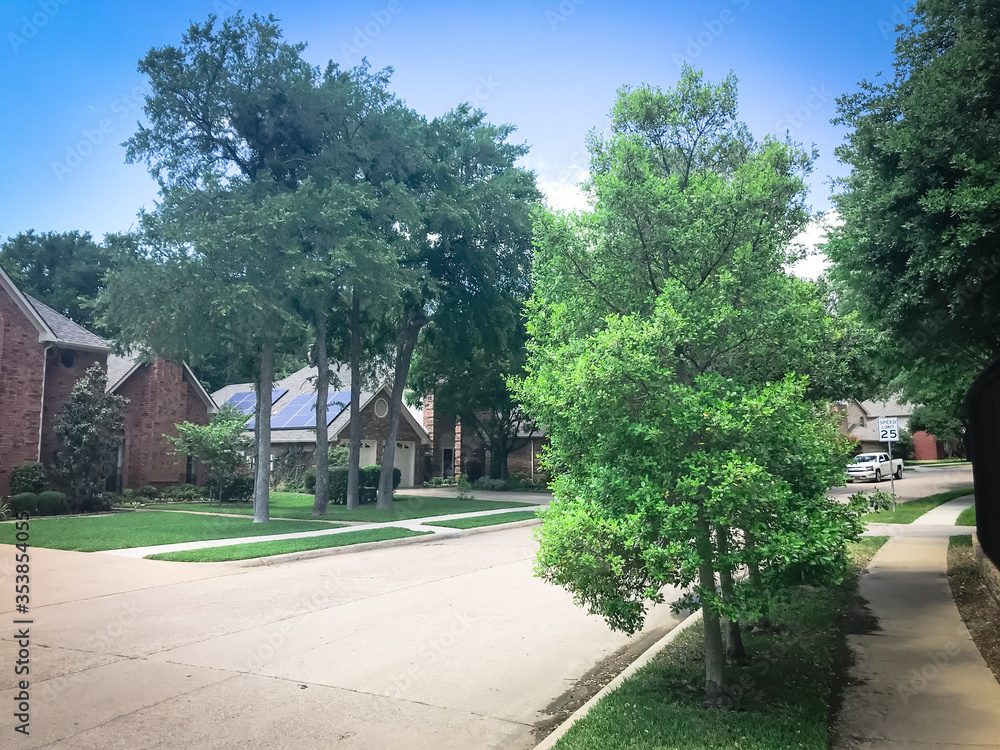 Fototapeta premium Lush green sidewalk pathway in residential area in suburban Dallas, Texas, USA and solar roof house