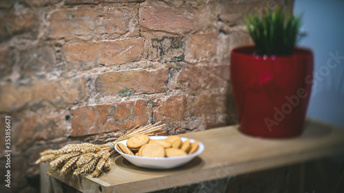 Close-up of plate with cookies on the wooden shelf. Modern loft interior. Brick wall. Decorative spikelets and flower.