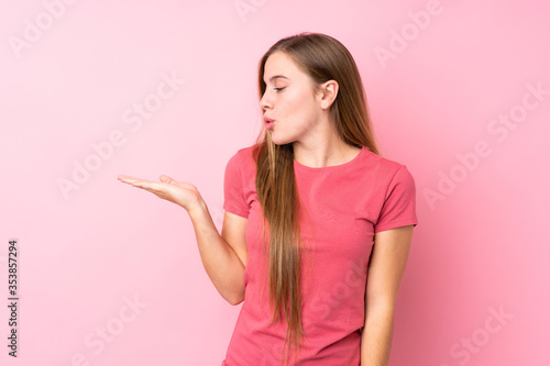 Teenager blonde girl over isolated pink background holding copyspace imaginary on the palm © luismolinero