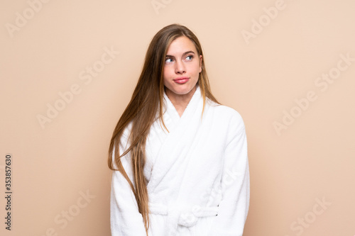 Teenager girl in a bathrobe over isolated background standing and looking to the side
