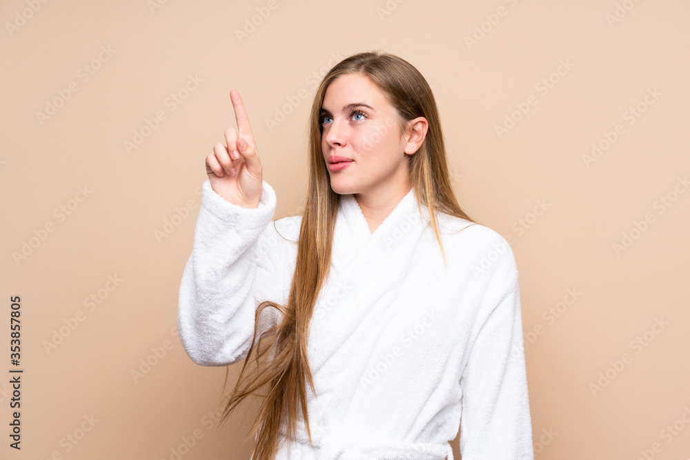 Teenager girl in a bathrobe over isolated background touching on transparent screen Teenager girl in a bathrobe over isolated background touching on transparent screen