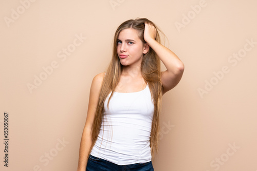Teenager blonde girl over isolated background having doubts