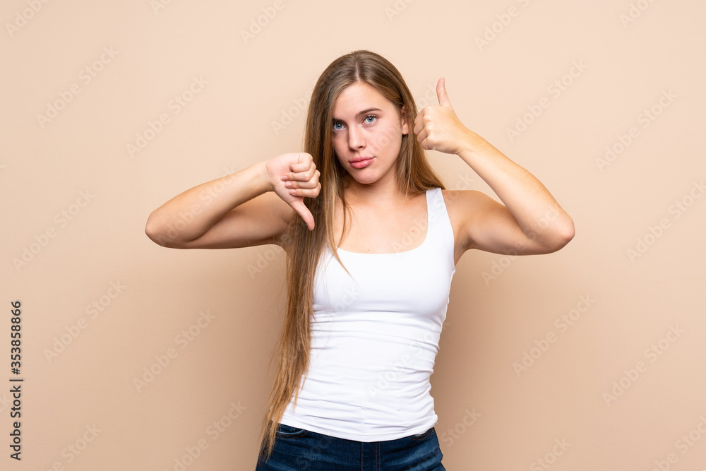 Teenager blonde girl over isolated background making good-bad sign. Undecided between yes or not Teenager blonde girl over isolated background making good-bad sign. Undecided between yes or not