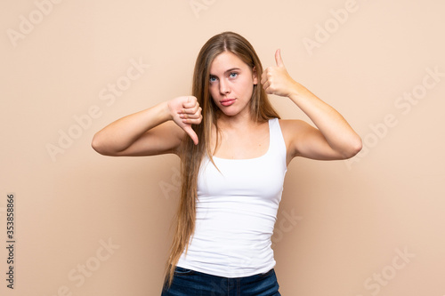 Teenager blonde girl over isolated background making good-bad sign. Undecided between yes or not