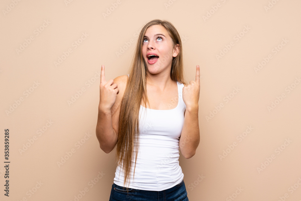 Teenager blonde girl over isolated background surprised and pointing up Teenager blonde girl over isolated background surprised and pointing up