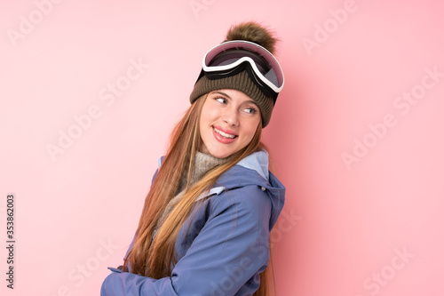 Skier teenager girl with snowboarding glasses over isolated pink background laughing