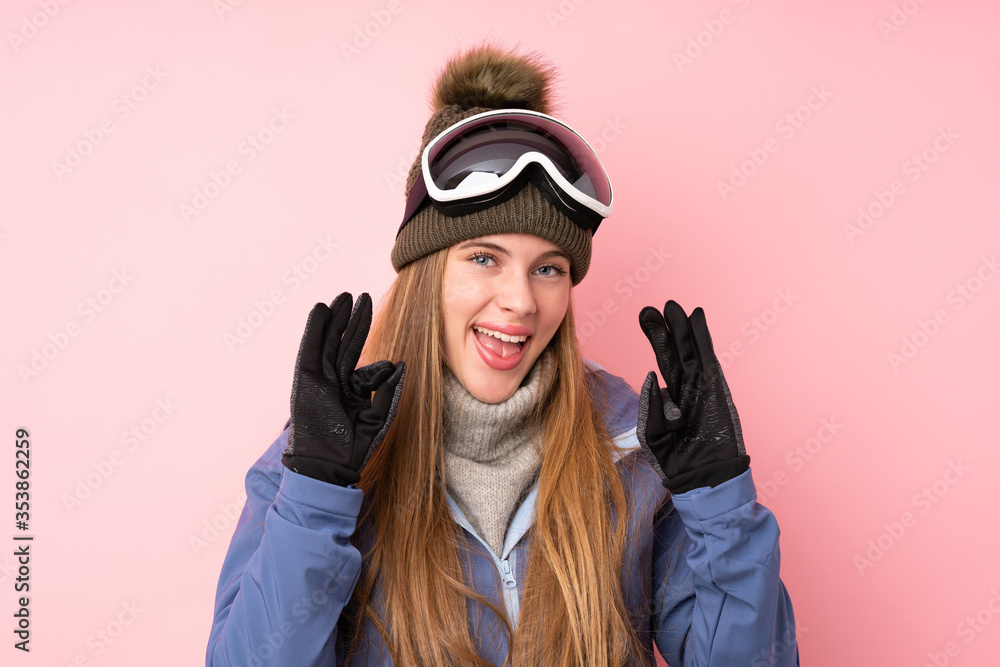 Skier teenager girl with snowboarding glasses over isolated pink background showing an ok sign with fingers
