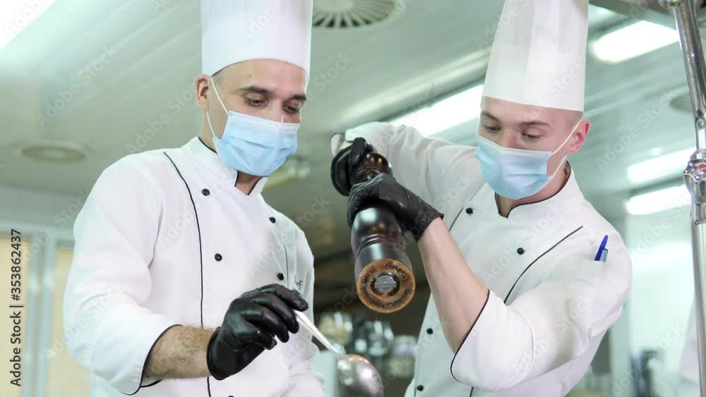 Chefs in protective masks and gloves prepare food in the kitchen of a restaurant or hotel Chefs in protective masks and gloves prepare food in the kitchen of a restaurant or hotel