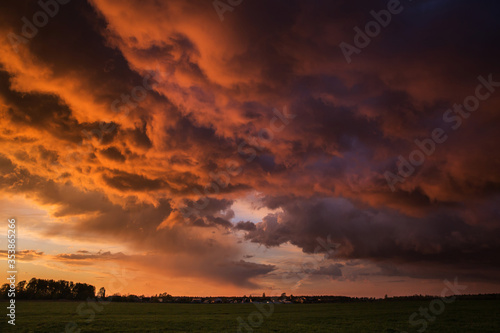 Landscape with majestic colorful dramatic red sky with fluffy clouds at sunset before before a thunderstorm and rain with the spacious field.
