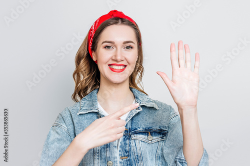 Student girl in denim jacket, bandana smiles and points to her left hand isolated on gray background, left-handed woman celebrating left-handed day photo