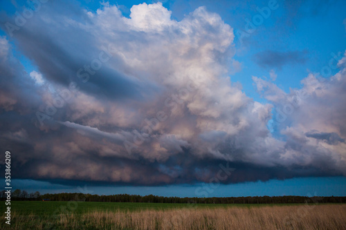 Landscape with majestic colorful dramatic red sky with fluffy clouds at sunset before before a thunderstorm and rain with the spacious field.