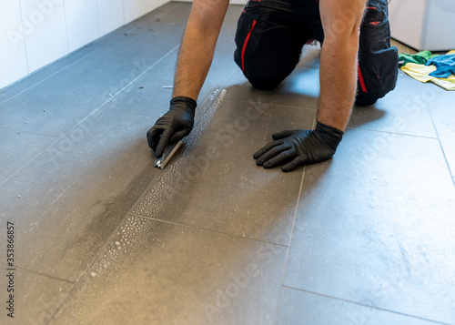 Fotografie professional cleaner cleaning grout with a brush blade and foamy soap on a gray