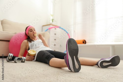 Lazy young woman eating ice cream instead of training at home, focus on legs
