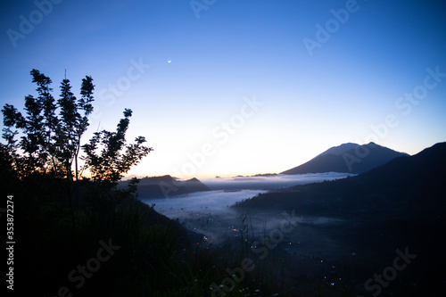 Blue hour during sunrise on top of the hill overlooking village with mist