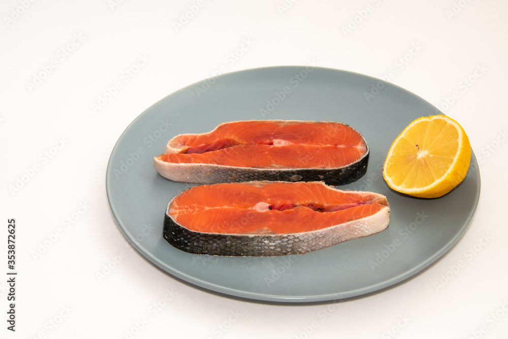 Raw salmon red fish steak with lemon slice on a plate, isolated on white background Raw salmon red fish steak with lemon slice on a plate, isolated on white background