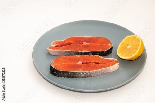 Raw salmon red fish steak with lemon slice on a plate, isolated on white background