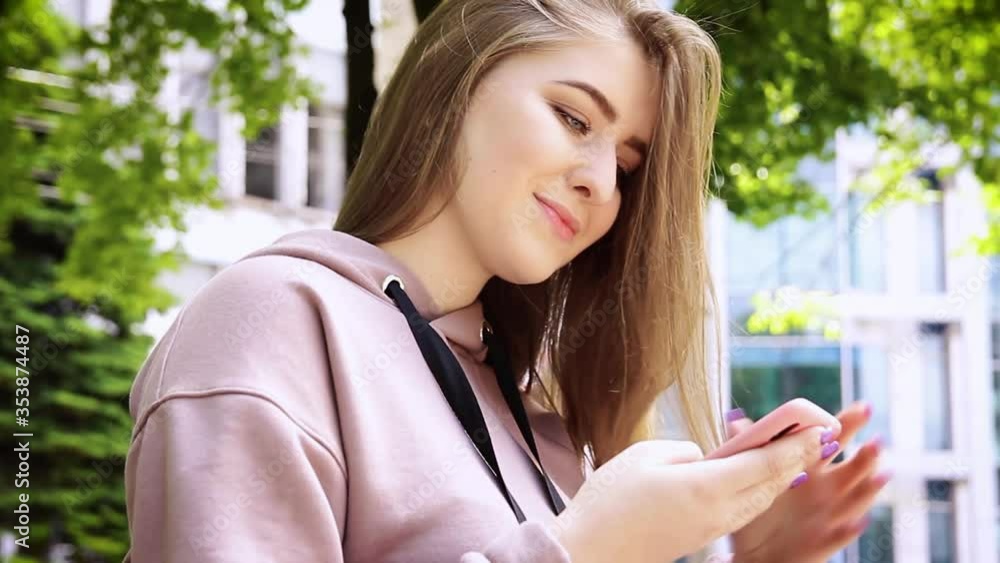 Young blond woman chatting on mobile phone sitting on the bench in park.