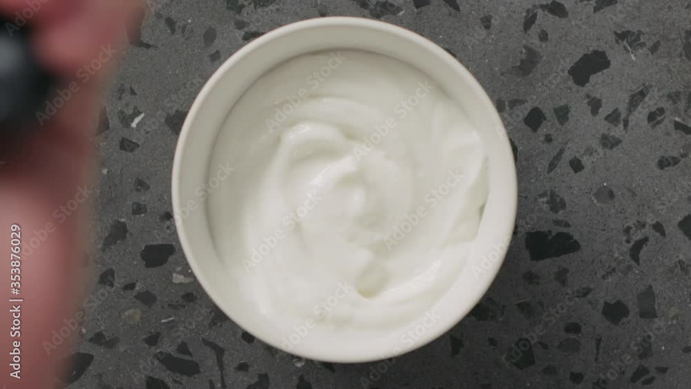 Slow motion top view blueberries fall into greek yogurt in white bowl on concrete background Slow motion top view blueberries fall into greek yogurt in white bowl on concrete background