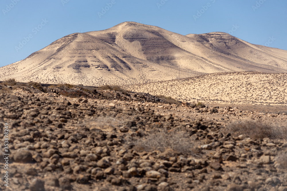 Halde voller dunklem Lavagestein auf weißem Sand in einer wüstenartigen Umgebung mit Hügelkette im Hintergrund