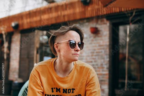 Bild auf Leinwand Sexy blonde young woman with short hair in sunglasses posing in the yard over brick wall background
