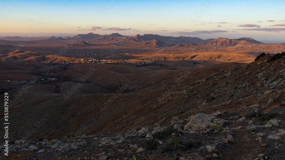 Letztes Sonnenlicht fällt auf eine hügelige Wüstenlandschaft mit Bergen, Tälern und Siedlungen