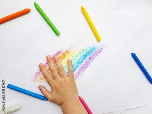 Colored wax crayons on white paper. A rainbow drawn by children's hands.