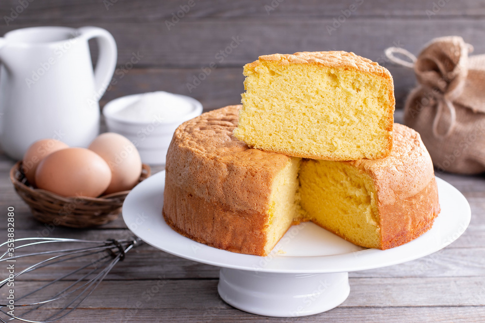 Homemade round sponge cake or chiffon cake on white plate so soft and delicious with ingredients: eggs, flour, milk on wood table Homemade round sponge cake or chiffon cake on white plate so soft and delicious with ingredients: eggs, flour, milk on wood table