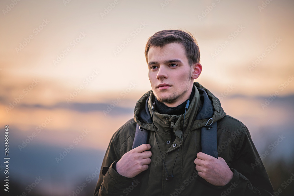 portrait of a guy with a backpack on nature against the evening sky	