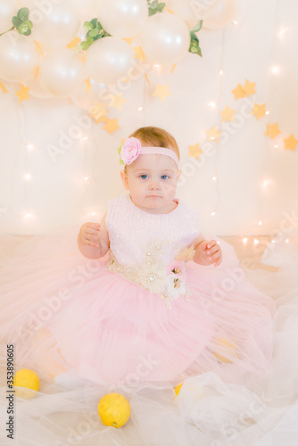 Cute little girl in a pink princess dress with a flower on her hair plays with wooden ballerinas among the golden stars on the background of a large white wooden moon and balloons. Children's decor. 
