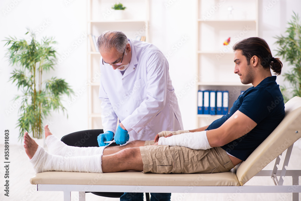Obraz premium Young injured man visiting old doctor traumatologist