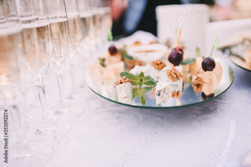 Assorted cheese on a plate: parmesan, brie, blue cheese, grapes. Reception, catering, clean dishes, glasses with champagne. The table is covered with a white tablecloth.