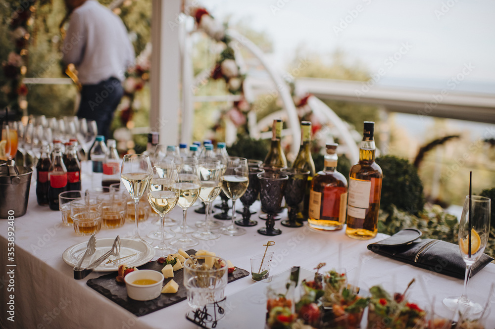 Glasses and bottles with white wine, whiskey. Plate with assorted cheese. Reception, catering. The table is covered with a white tablecloth. Glasses and bottles with white wine, whiskey. Plate with assorted cheese. Reception, catering. The table is covered with a white tablecloth.