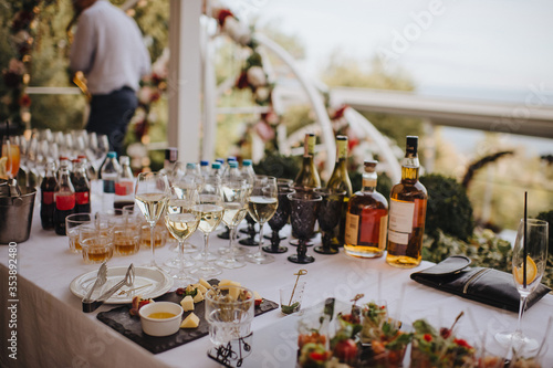 Glasses and bottles with white wine, whiskey. Plate with assorted cheese. Reception, catering. The table is covered with a white tablecloth.