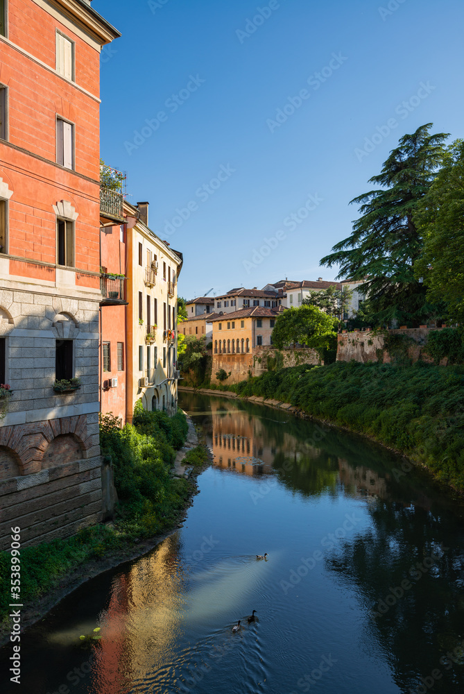 A short distance from Piazza dei Signori, the Retrone river passes under the San Paolo bridge. The buildings are reflected in the dark blue water where Mallards couples swim. Vicenza, Italy.
